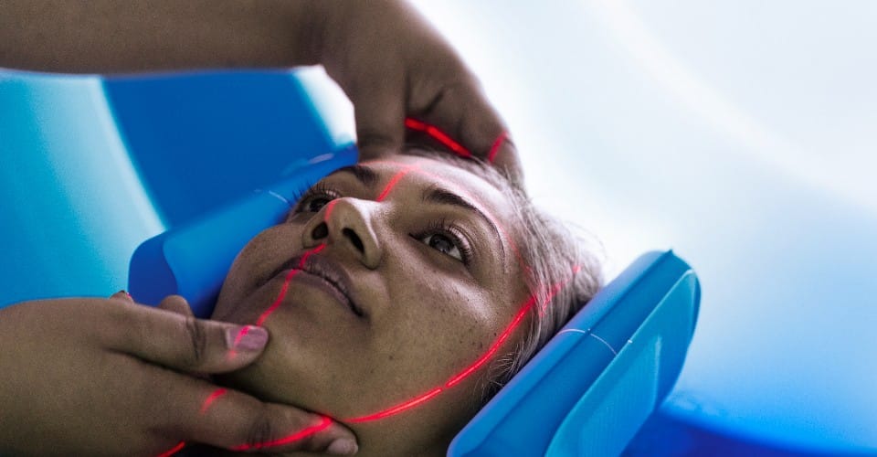 A female patient is aligned correctly in a medical device by an attending healthcare professional.